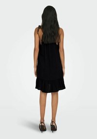 Vestido negro sin mangas con un dobladillo con volantes, hecho de una tela ligera. Cuenta con tirantes ajustables y un corte relajado.