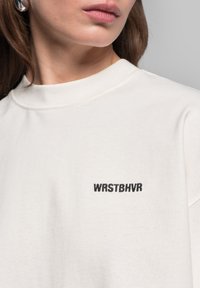 Crème-kleurige katoenen sweatshirt met een ronde halslijn, korte mouwen en een zwart geborduurd logo "WRSTBVR" op de linkerborst.