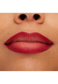 Rød leppestift påførte på fyldige lepper, med en jevn tekstur. Den underste leppen er litt fyldigere, og hudtonen er varm.