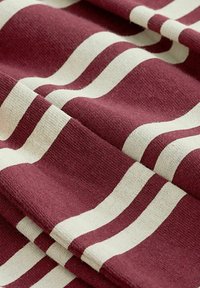 Burgundy- och krämrandig tyg med en texturerad yta; har vågiga linjer och ett mjukt, vävt utseende, arrangerat i veck.