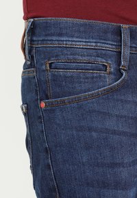 Jeans i mörkblå denim med orange sömmar, med en liten röd etikett, rak passform och en fickdesign på framsidan.