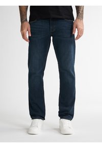 Jeans de mezclilla azul oscuro con corte recto, que cuentan con cinco bolsillos, costuras sutiles y una textura suave, combinados con zapatillas blancas.
