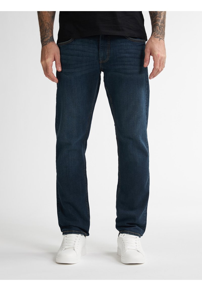 Jeans de mezclilla azul oscuro con corte recto, que cuentan con cinco bolsillos, costuras sutiles y una textura suave, combinados con zapatillas blancas.