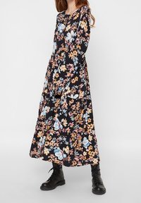 Blommig maxiklänning med svart bas och flerfärgade blommor, långa ärmar och en lös silhuett som matchas med svarta kängor.