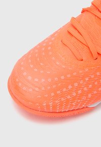 Lys orange sportssko med tekstureret strikket overdel, med hvide prikkede mønstre og matchende snørebånd, designet til letvægtsydelse.