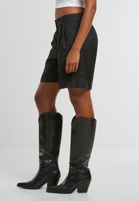 Černé saka šortky s záhyby spárované s černými koženými vysokými botami na podpatku, které mají elegantní design a hladkou texturu.