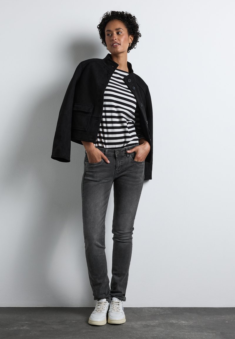 Černá zamšová krácená bunda, pruhované černo-bílé tričko, tmavě šedé slim džíny a bílé tenisky s texturedními podrážkami.