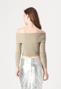 Ribbet, avkortet topp med avdekket skuldre i lys beige, med lange ermer og en kort hem, kombinert med en skinnende sølvskjørt.