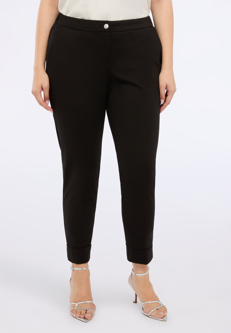 Pantaloni negri ajustați, cu o croială slim,  clinciuri la glezne, textură netedă și închidere cu un buton frontal, asortați cu tocuri argintii.