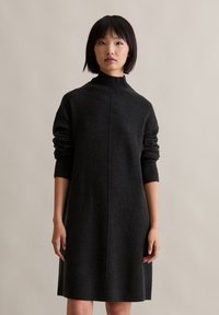 Temno siva pletena obleka z visokim ovratnikom, dolgimi rokavi in sproščenim krojem. Ima rebraste manšete in osrednji šiv.