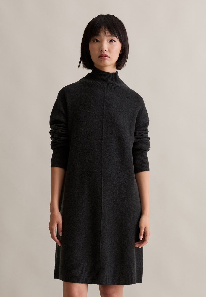 Temno siva pletena obleka z visokim ovratnikom, dolgimi rokavi in sproščenim krojem. Ima rebraste manšete in osrednji šiv.