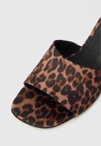 Sandaler med åben tå i leopardprint, prydet med en brun satinfinish og sorte pletter, med en bred overdel og flad sål.