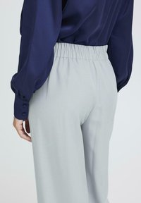 Šviesiai pilkos kelnės su elastine juosmena, derinamos su tamsiai mėlyna satino ilgomis rankovėmis palaidine. Akivaizdus minkštas tekstūros ir laisvas pritaikymas.