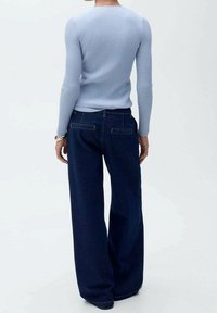 Top de manga larga de color azul claro con canalé, combinado con jeans de pierna ancha de mezclilla oscura, que presentan un diseño clásico y detalles de costura simples.