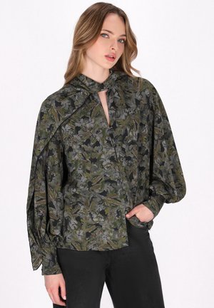Bluză florală verde cu decolteu în formă de cheie, mâneci lejere și textură mătăsosă. Modelul prezintă frunze în nuanțe mai închise pe un fundal negru.