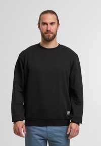 Zwarte sweatshirt met een ronde halslijn en lange mouwen. Gemaakt van een gladde stof, met een geribde zoom en een klein logootje aan de onderkant.