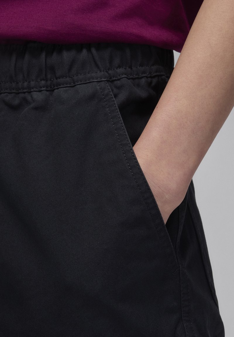 Pantalones cortos de algodón negros con una cintura elástica, que presentan bolsillos laterales y una textura suave y mate. La prenda muestra detalles de costura mínimos.