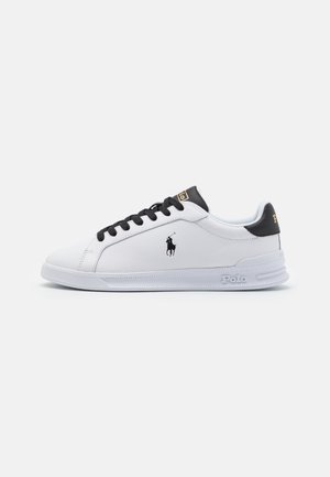 Baskets basses blanches avec lacets noirs, languette de talon noire, logo Polo sur le côté, et "Polo" embossé sur la semelle blanche.