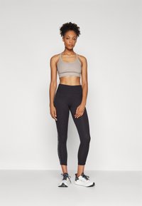 Light gray sports bra and black leggings with side branding. The leggings are form-fitting and cropped above the ankle. White sneakers.