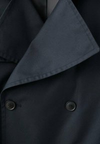 Abrigo azul marino de doble botonadura con cuello ancho, que presenta una textura de tela suave y dos botones negros en la parte delantera.