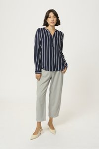 Blusa a rayas marinas con una placket de botones parcial y mangas largas, combinada con pantalones tapered en gris claro y tacones de punta crema.