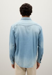 Camicia di jeans in azzurro chiaro, con colletto a punta, maniche lunghe con polsini abbottonati e un orlo leggermente curvo. Texture liscia.