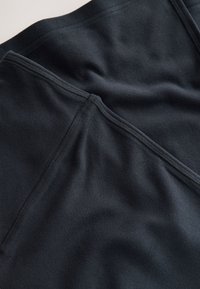 Tela negra texturizada con un acabado suave, que presenta costuras planas y un aspecto ligeramente arrugado. Diseñada para un uso cómodo.