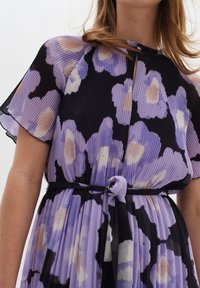 Violet kukkaelinen mekko, jossa on laskostettu pinta, lyhyet kaarrokkeet, mustat yksityiskohdat ja kankainen vyö vyötäröllä.