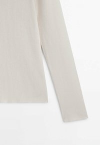 Top à manches longues gris clair en tissu côtelé. Il présente un col rond et un ajustement près du corps avec des lignes texturées sur l'ensemble du matériau.