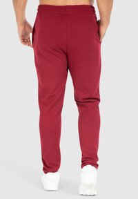 Burgundy joggers met een drawstring tailleband, zijzakken en tapse benen, gemaakt van zachte katoenmix stof, gecombineerd met witte sneakers.