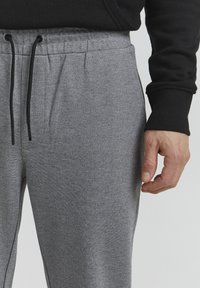 Grå atletiske joggingbukser lavet af blød stof, med en elastisk linning og snoretræk samt sidelommer. Tekstureret, åndbart materiale.