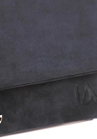 Clutch de ante negro con una textura suave, que presenta un diseño plegado y un acento en tono plateado. Detalle sutil de logo en relieve visible.