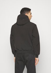 Giacca nera con cappuccio caratterizzata da una vestibilità comoda, polsini e orlo elasticizzati, con una texture liscia e un design minimalista.