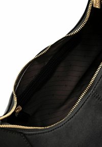 Interno di una borsa in suede nera con una zip dorata. Foderato con un tessuto scuro che presenta motivi sottili e ripetuti. Visibili più scomparti interni.