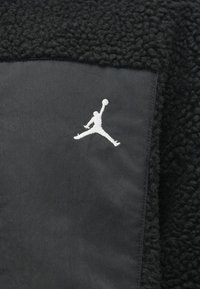 Fekete gyapjúdzseki, fekete nylon résszel és fehér Jumpman logóval. Texturált anyag, puha felülettel, kontrasztos sima felülettel.