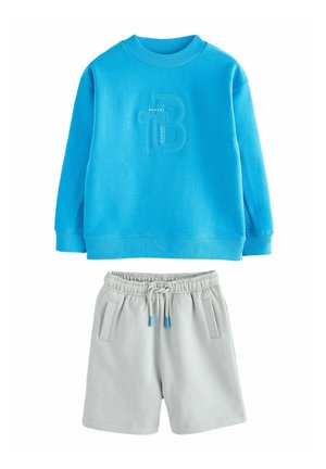 Blauer Kapuzenpullover mit geripptem Kragen und eingeprägtem Logo, kombiniert mit hellgrauen Shorts mit elastischem Bund und seitlichen Taschen.