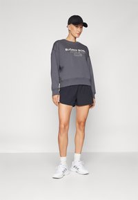 Sudadera gris con el texto "BJÖRN BORG ATHLETIC CLUB", combinada con pantalones cortos deportivos negros y zapatillas blancas, con tejidos texturizados y un corte relajado.