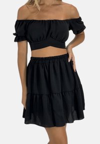 Zwart tweedelig set met een off-shoulder cropped top met geruite mouwen en een gelaagde rok met elastische taille. Zachte, gestructureerde stof.