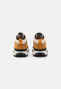 Zapatillas de ante marrón y malla con suela negra, que presentan un acento naranja en el talón y un cuello acolchado.