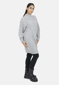 Lys grå strikket sweaterkjole med høj hals, ribbet tekstur og oversized ærmer, parret med sorte leggings og kampstøvler.