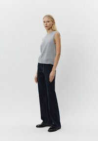 Top gri fără mâneci, cu un croi lejer, purtat cu pantaloni largi de culoare albastră închis, cu cusături galbene în contrast. Pantofi negri completează ținuta.