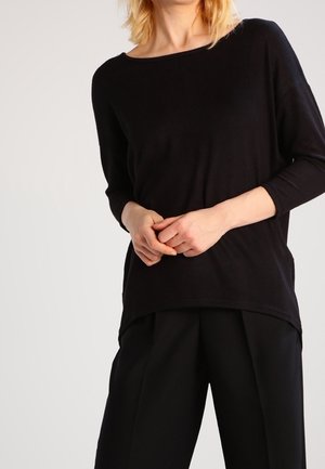 Maglione nero con scollatura ampia e maniche a tre quarti, realizzato in un tessuto morbido e testurizzato, abbinato a pantaloni neri sartoriali.