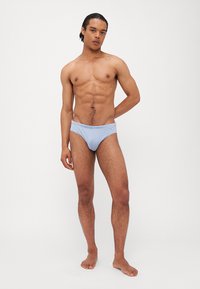 Svetlo modre plavalne hlačke z gladko teksturo, elastičnim pasom in diskretno oznako. Oblikovanje nudi tesno prileganje.