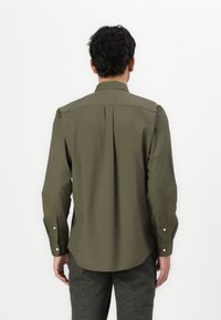 Camicia a maniche lunghe verde oliva con piega posteriore, colletto a punta e polsini con bottoni. Il tessuto appare liscio con una trama leggera.