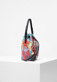 Borsa a secchiello astratta e colorata con motivo, dotata di tracolla nera regolabile e lacci con pon-pon, posata su un piedistallo bianco contro uno sfondo neutro.