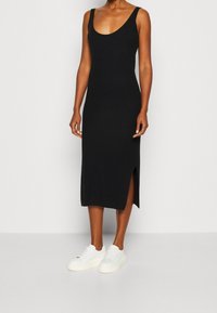 Czarna prążkowana sukienka midi z dekoltem typu scoop i szerokimi ramiączkami, z bocznym rozcięciem ułatwiającym ruch, zestawiona z białymi tenisówkami.