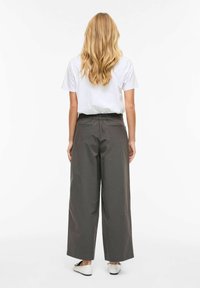 Pilkos plačios kojinės kelnės su tampria liemene, matomos iš nugaros. Komplektą užbaigia balta trumpomis rankovėmis palaidinė. Tekstūruota medžiaga.