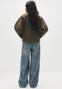 Oversized brown sweater with dropped shoulders paired with wide-leg, lightly distressed blue denim jeans featuring paint splatter patterns.