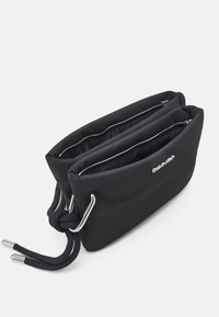 Černá nylonová taška se dvěma zipovými odděleními, s kovovými doplňky a uzlovými rukojeťmi. Hladký povrch, minimalistický design.