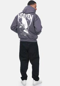 Grå hættetrøje med ryggrafik af en due, pigtråd og teksten "HEAVEN". Kombination med sorte bukser og hvide sneakers. Blødt stof, afslappet pasform.
